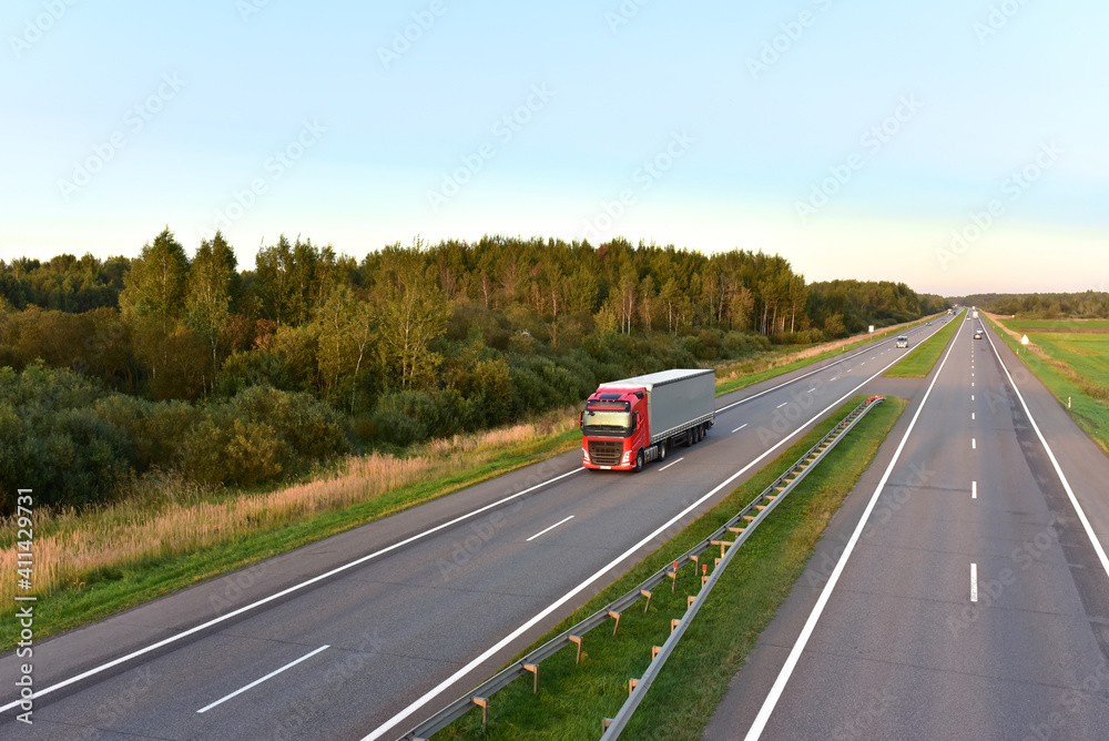 Truck with semi-trailer driving along highway on the sunset background. Goods delivery by roads. Services and Transport logistics. Soft focus. Truck with semi-trailer driving along highway on the sunset background. Goods delivery by roads. Services and Transport logistics. Soft focus.