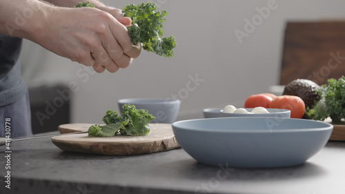 man make salad with kale, mozzarella, avocado and cherry tomatoes, tear kale