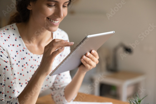 Close up of smiling young woman look at table screen shopping online on modern device from home. Happy millennial female work distant or study on internet on pad gadget. Technology concept.