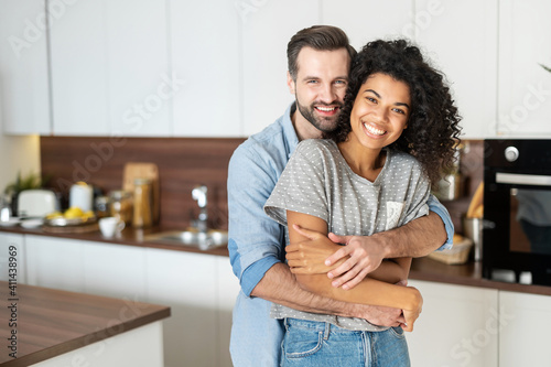 Bild auf Leinwand Sweet multi-ethnic couple in love stands in embraces in the kitchen