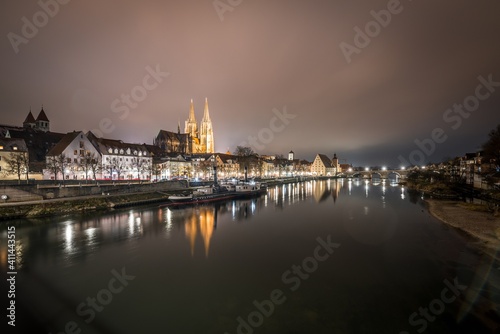 Blick zu der steinerne Brücke in Regensburg nachts im Nebel über den Fluss Donau mit dem beleuchteten Dom und historischer Altstadt , Deutschland