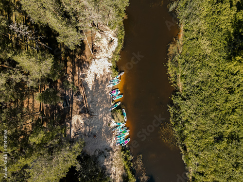 Lots of colorful SUP stand up paddle boards near river riverside on a sunny summer day. View from the drone