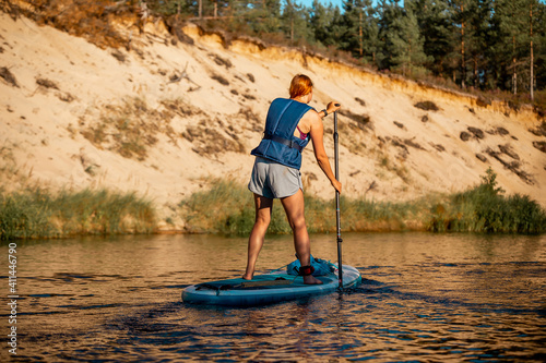 Woman do SUP stand up paddle boarding in river. Rear view