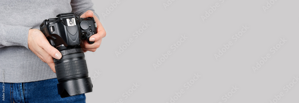 Hand with black photo camera on grey background.