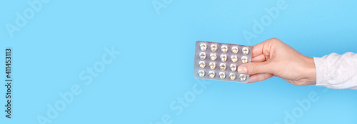 Hand with pills in blister on blue background.