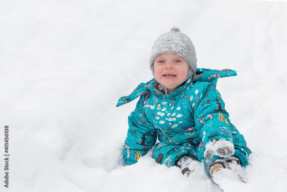 Cute little boy happily playing in the white fluffy fresh snow outdoors in winter. The child tries to take a snowball. Childhood. Game Cute little boy happily playing in the white fluffy fresh snow outdoors in winter. The child tries to take a snowball. Childhood. Game