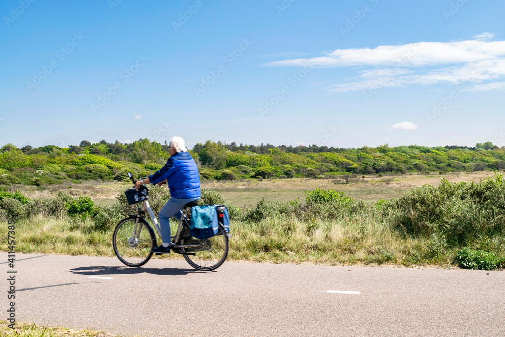 Active recreation during sea vacation. Sports retirees. An elderly pensioner rides a bicycle on the road between the dunes on the coast in the Netherlands. 