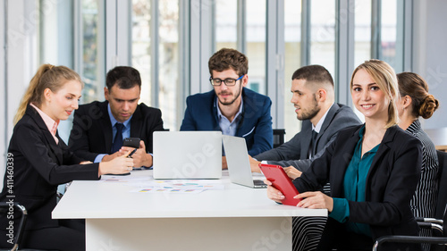 Group portrait of six business people team sitting and talking in conference together in an office and while the woman boss sit on the top of table. Idea for success of teamwork in modern business