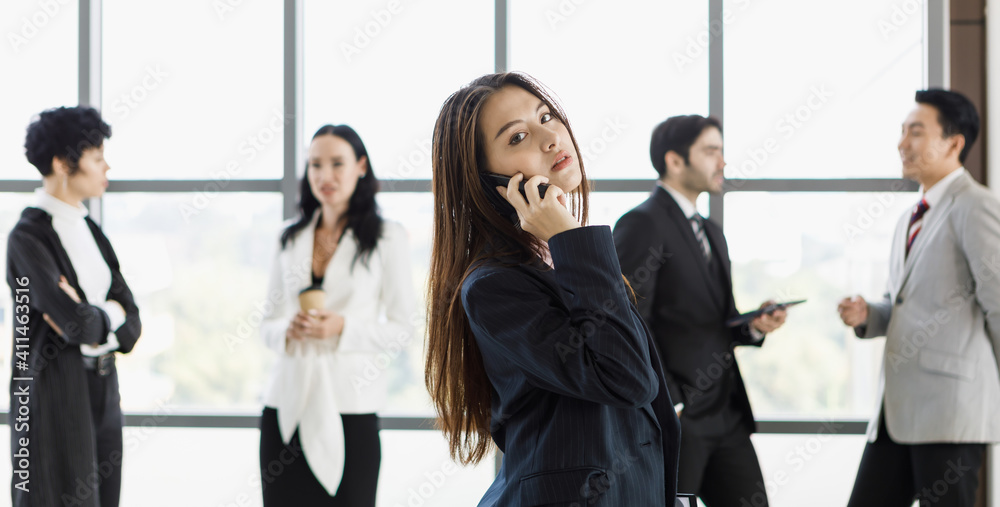 Cute Asian businesswoman using and talking on phone in front of diverse group of businesspeople. Cute Asian businesswoman using and talking on phone in front of diverse group of businesspeople.