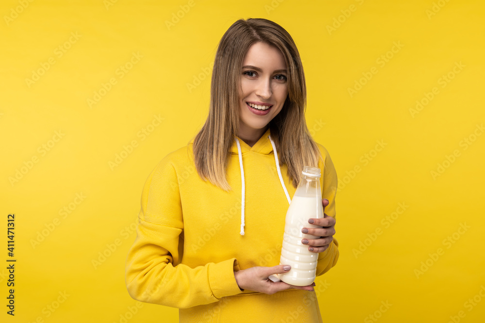 Photo of attractive lady holds bootle of milk, feels nice about dairy products. Wears casual yellow hoody, isolated yellow color background Photo of attractive lady holds bootle of milk, feels nice about dairy products. Wears casual yellow hoody, isolated yellow color background