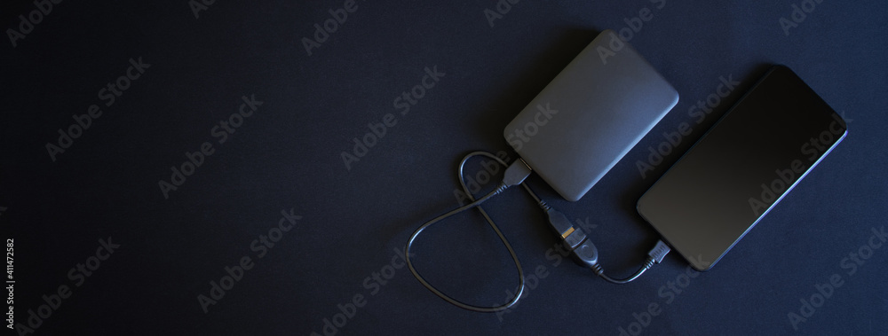 A smartphone and an external hard drive connected to it with an OTG cable lie on a black background. Free space for an inscription A smartphone and an external hard drive connected to it with an OTG cable lie on a black background. Free space for an inscription