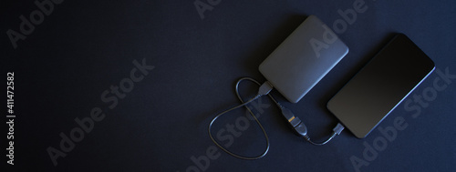 A smartphone and an external hard drive connected to it with an OTG cable lie on a black background. Free space for an inscription