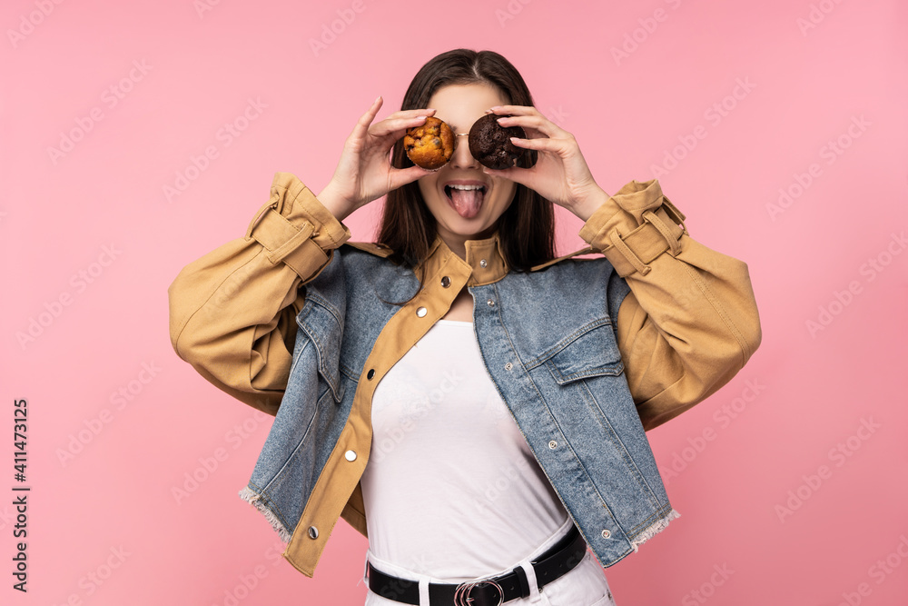 Fototapeta premium Photo of attractive lady covered eyes with muffins fun, wear casual jeans jacket white undershirt isolated pink color background