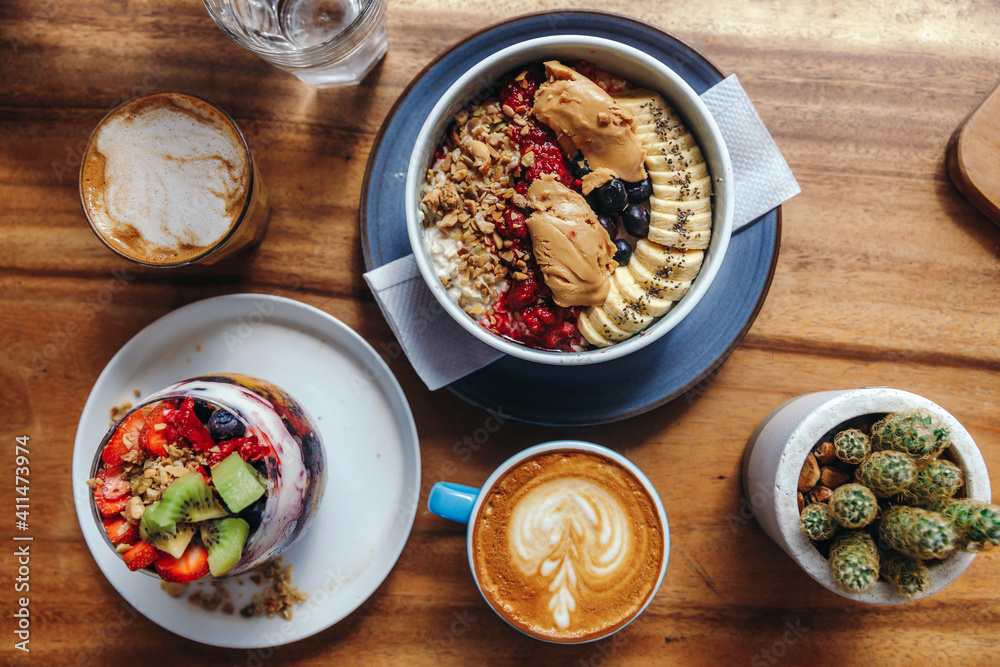 Healthy breakfast with chia strawberry pudding, oatmeal bowl with banana, peanut butter, blackberries, raspberries, nuts, seeds and goji berries and a cup of hot soybeans cappuccino