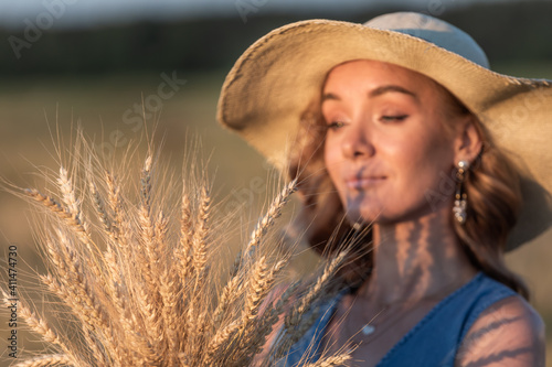 Girl in a wide-brimmed hat on a wheat field in the rays of the setting sun © alexkazachok