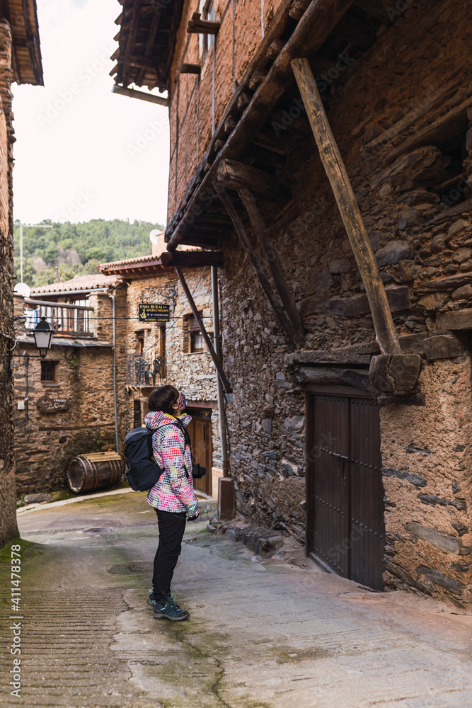 Young and attractive female with a colourful jacket standing and witnessing the architecture of a small and ancient village.