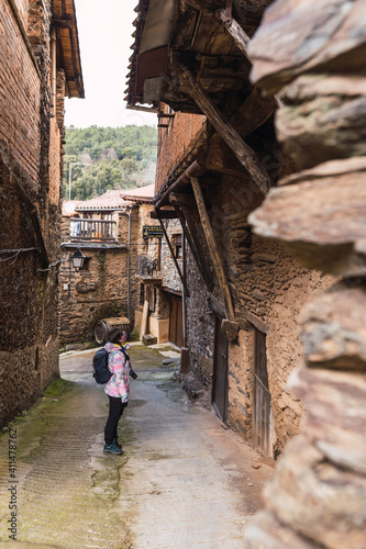 Young and attractive female with a colourful jacket standing and witnessing the architecture of a small and ancient village.