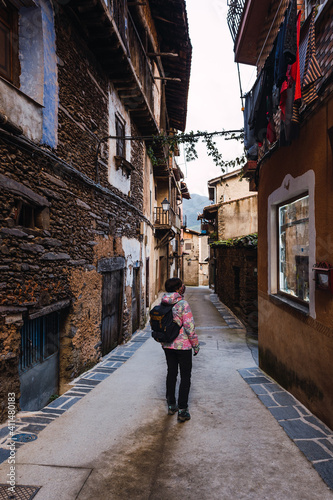Young and attractive female with a colourful jacket standing and witnessing the architecture of a small and ancient village.