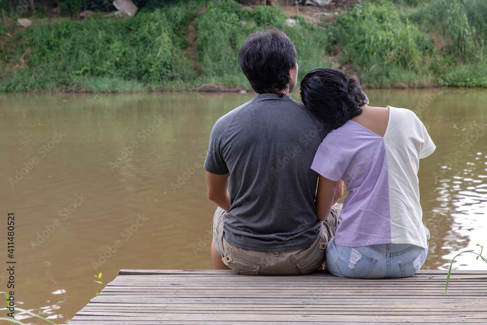 Rear view of young couple sitting in the border of a canal and watching river movement with together. Selective focus. Rear view of young couple sitting in the border of a canal and watching river movement with together. Selective focus.