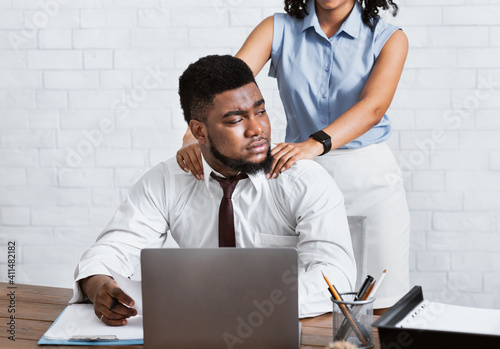 Lady boss sexually molesting her attractive male subordinate, putting hands on his shoulders at company office photo