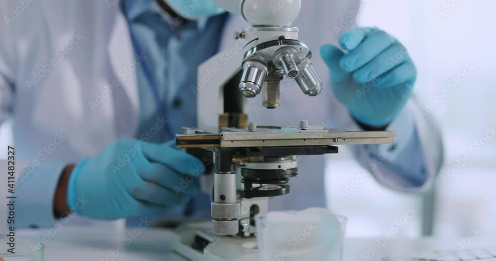 Medical laboratory. Young scientist examining microbiology tests developing vaccine with microscope working at office. Quarantine. Pandemic.