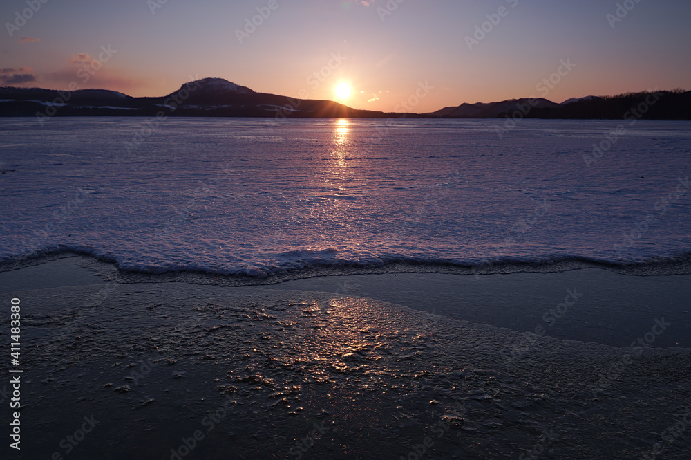 夜明けの冬の湖の湖面の氷を照らす朝陽。日本の北海道の屈斜路湖。
