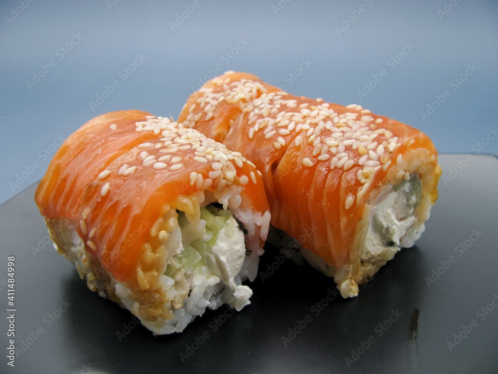 Philadelphia sushi with cheese and cucumbers on a black plate on a blue background. Philadelphia sushi with cheese and cucumbers on a black plate on a blue background.