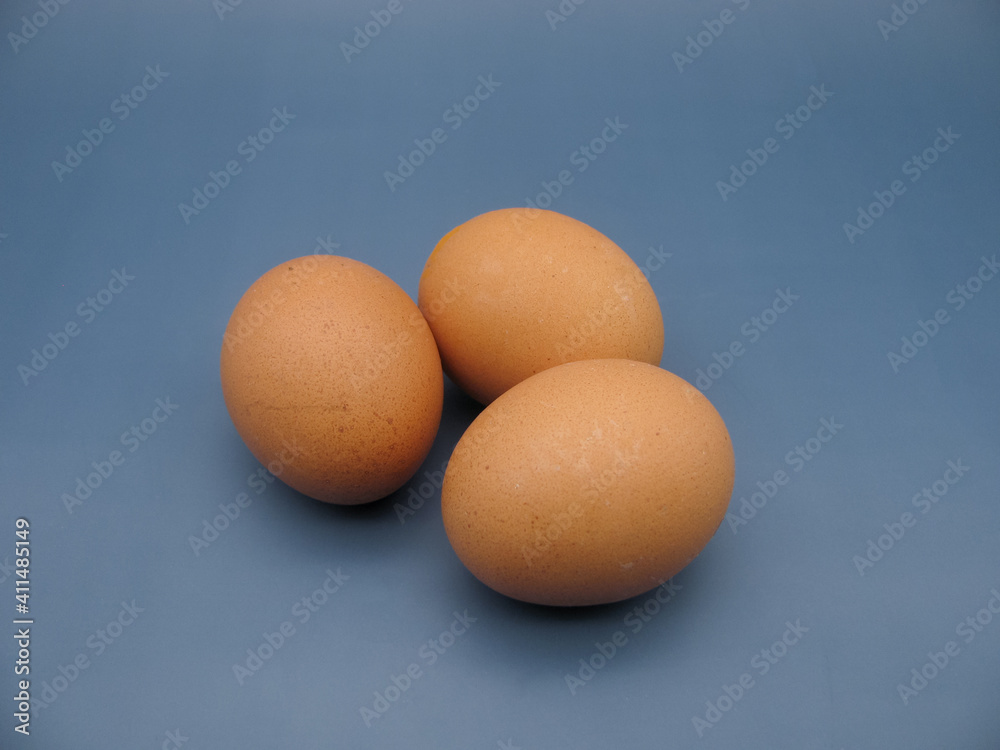 three brown raw chicken eggs on a blue background three brown raw chicken eggs on a blue background