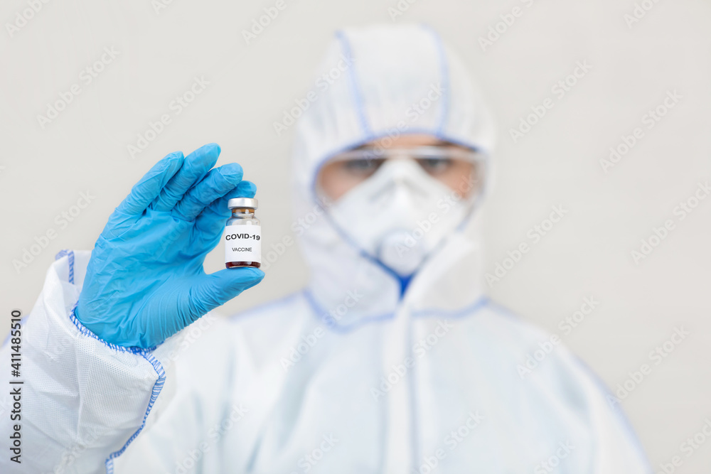 Medic in hazmat suit, gloves, protective mask and goggles holds vaccine against Covid-19 Medic in hazmat suit, gloves, protective mask and goggles holds vaccine against Covid-19