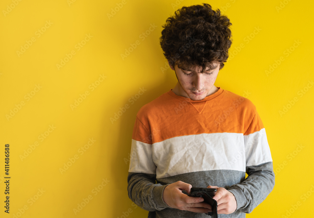 Cute brown curly haired boy with mobile phone on yellow studio background, he is using mobile applications or chatting with friends, copy space. Concept of using smartphone, addiction to gadgets. Cute brown curly haired boy with mobile phone on yellow studio background, he is using mobile applications or chatting with friends, copy space. Concept of using smartphone, addiction to gadgets.