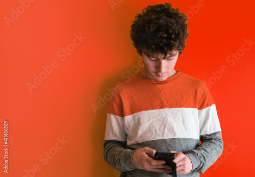 Cute brown curly haired boy with mobile phone on yellow studio background, he is using mobile applications or chatting with friends, copy space. Concept of using smartphone, addiction to gadgets. © Massimo Parisi