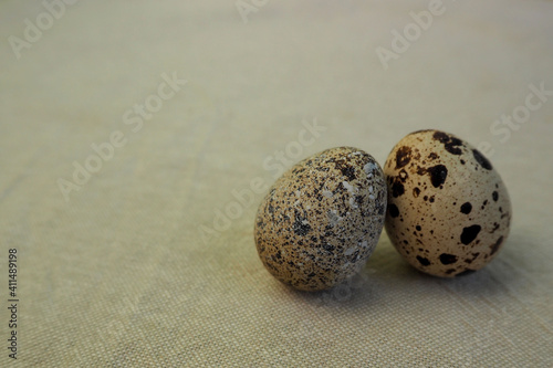 two raw quail eggs lie side by side on a light beige background side view . healthy eating