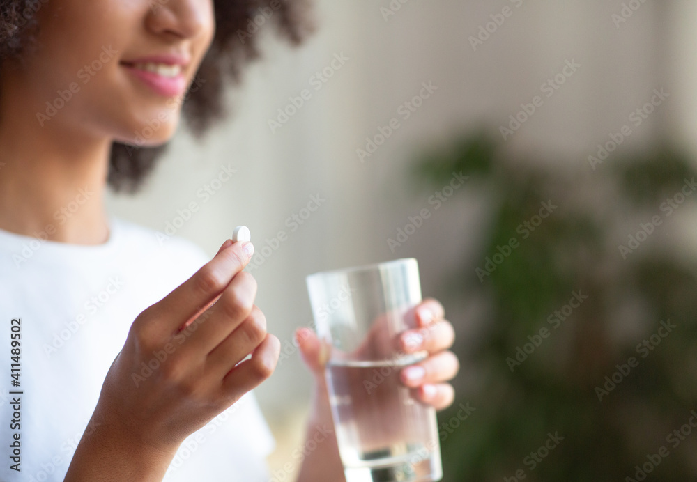 Smiling woman taking white round pill, holding water glass in hand Smiling woman taking white round pill, holding water glass in hand