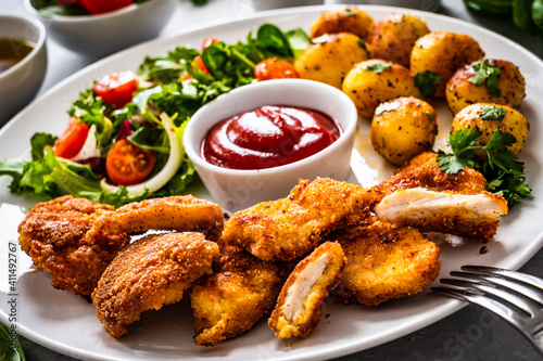 Fried breaded chicken nuggets with fried potatoes and fresh vegetables 