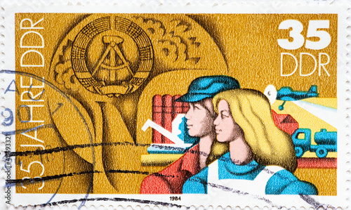  a postage stamp from Germany, GDR showing a portrait of a man and woman in work clothes in front of agricultural facilities and buildings with the GDR emblem. 35 years of the GDR