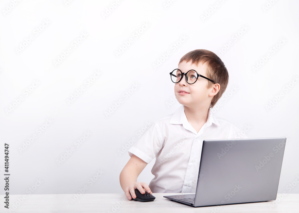 a boy with glasses, an elementary school student, sits at a table with a laptop on a white background a boy with glasses, an elementary school student, sits at a table with a laptop on a white background