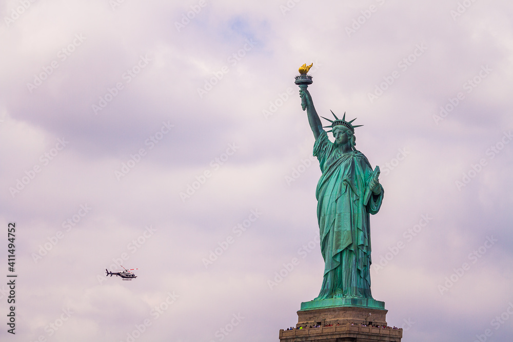 Statue of Liberty with a NYPD helicopter flying in the cloudy sky
