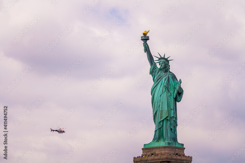 Fototapeta premium Statue of Liberty with a NYPD helicopter flying in the cloudy sky