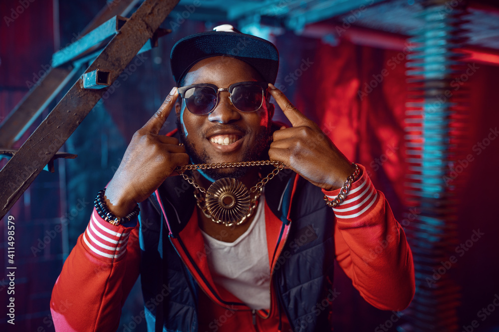 Smiling rapper with gold chain posing in studio - obrazy, fototapety, plakaty 