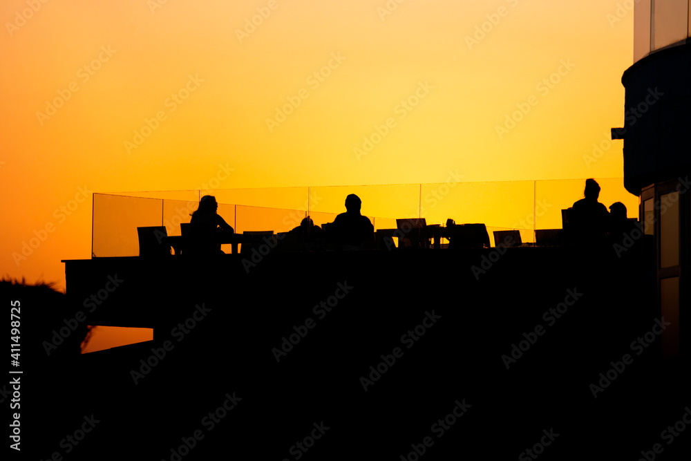 Peoples Silhouettes On Sunset Sit At Tables And Enjoy Summer Evening.