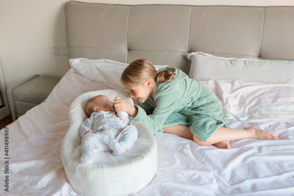 Little sister and her baby brother. Toddler kid playing with new sibling. Girl and baby 2-3 months old relax in a home bedroom. Family with two children at home. Love, trust and tenderness concept Little sister and her baby brother. Toddler kid playing with new sibling. Girl and baby 2-3 months old relax in a home bedroom. Family with two children at home. Love, trust and tenderness concept
