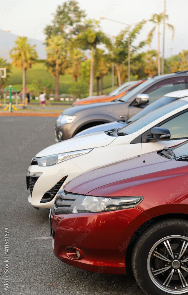 Closeup of front side of red car with other cars parking in outdoor parking area in twilight evening. Vertical view.