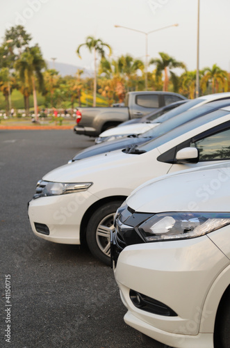 Closeup of front side of white car with other cars parking in outdoor parking area in twilight evening. Vertical view.