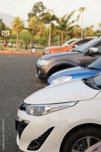 Closeup of front side of white car with other cars parking in outdoor parking area in twilight evening. Vertical view.