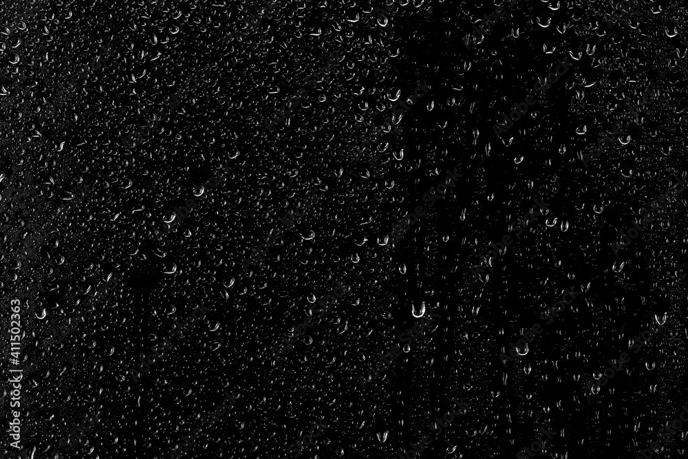 Obraz premium Drops of water flow down the surface of the clear glass on a black background. Texture for creativity.