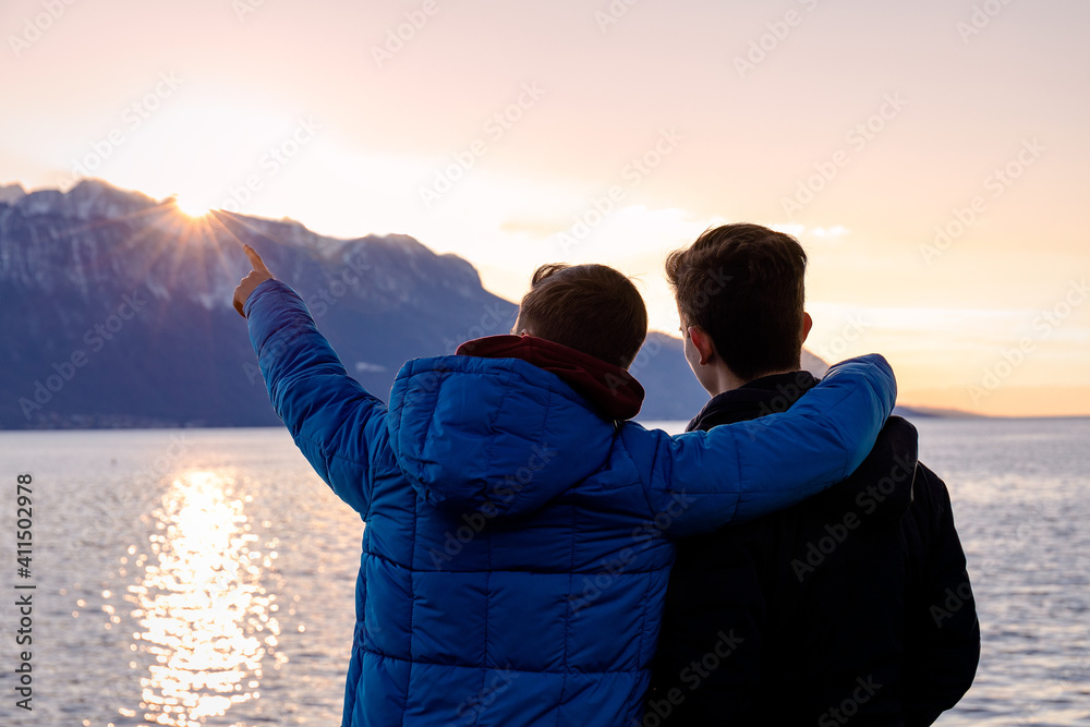 Brothers shaming a moment together while enjoying the sunset - the sun sinking behind the mountains on the lake’s edge.