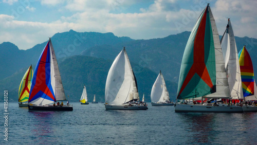 sail boat yacht race regatta with multi colorful spinnaker sails and mountain background