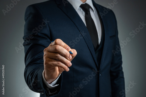 A man in a business suit holds out his hand with a ballpoint pen, writes in the air. Stock for business concept. Close-up, copy space.