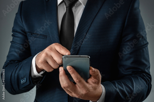 A businessman in a business suit holds a smartphone in his hands. Uses the Internet to work and communicate with partners. Online business concept, remote work, freelance. Close-up.