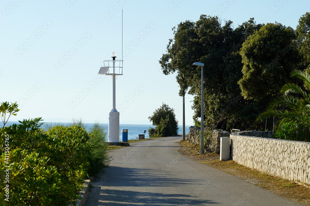Promenade by the sea with a small white lighthouse in a coastal village